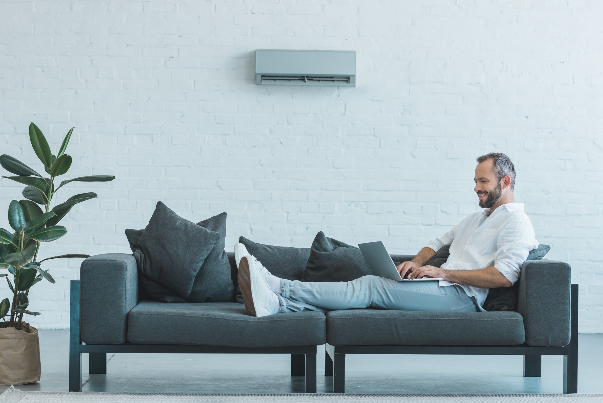 handsome-man-working-with-laptop-on-sofa-with-air-conditioner-on-wall-at-home.jpg